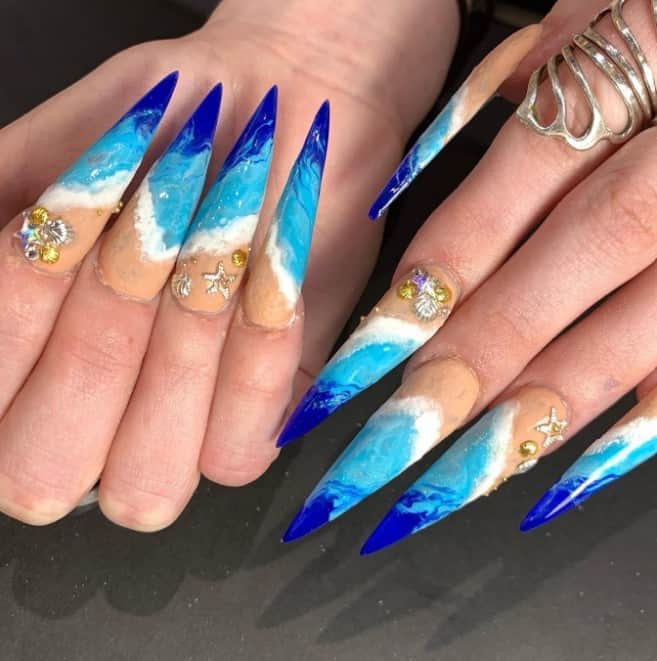 nails with two-toned blue waves, white seafoam, and creamy pale beige sand on long stiletto nails, then decorated with 3D shells