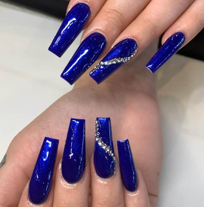 A woman's hands with royal blue nail designs with rhinestones