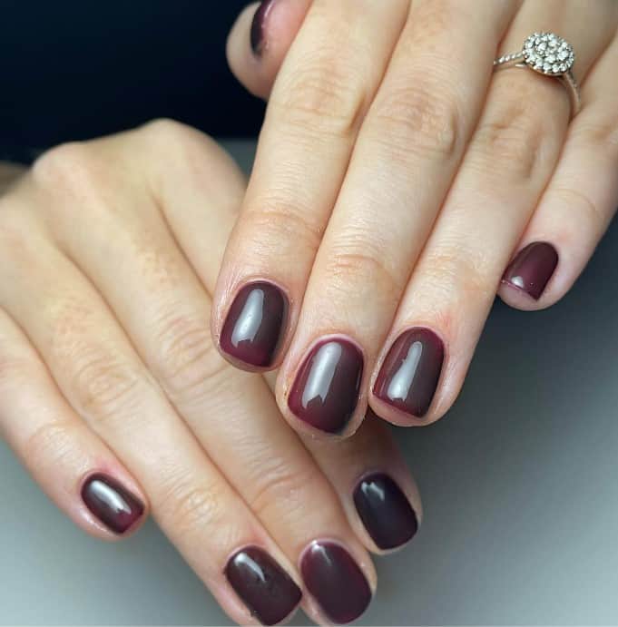 A woman's hands with nails drenched in a deep burgundy color and made to shine with a luscious gloss