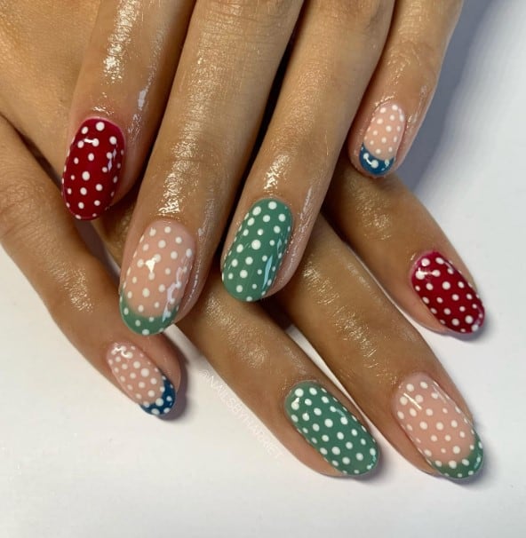 A woman's hands with deep green, red, and blue and polka dots nails design