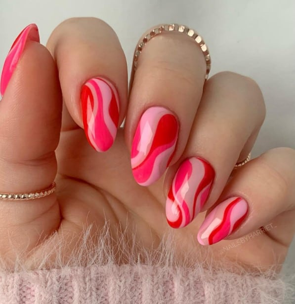 A woman's hand with a pink and red nails with swirls on a pale pink base