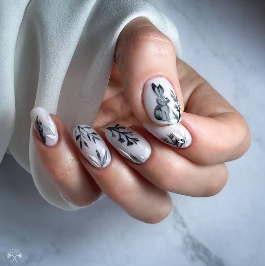 A woman holding up a hand with a black and white nail design featuring detailed plant designs and an intricate bunny sketch