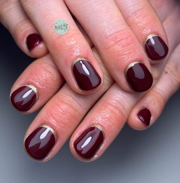 A woman's hands with rich burgundy hue on short nails perfectly accented by gold cuticle cuffs