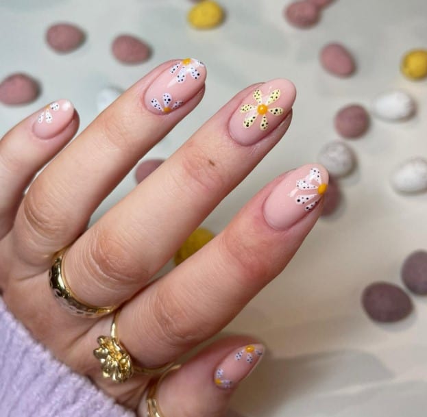 A woman's hand is painted with pastel colors and speckled patterns to decorate flower petals on nude nails