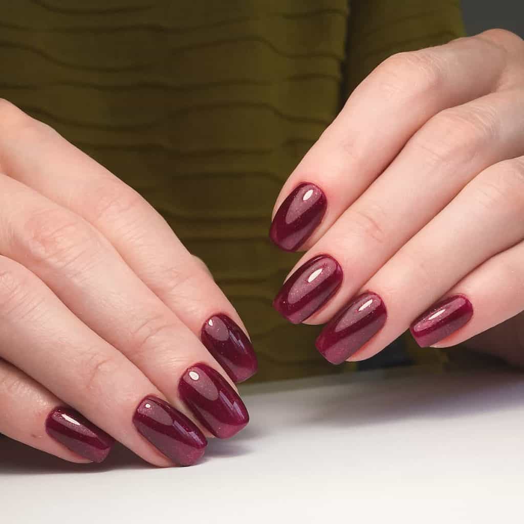 A woman's hands with mid-length square nails that twinkle in a glittery burgundy hue with a clear top coat