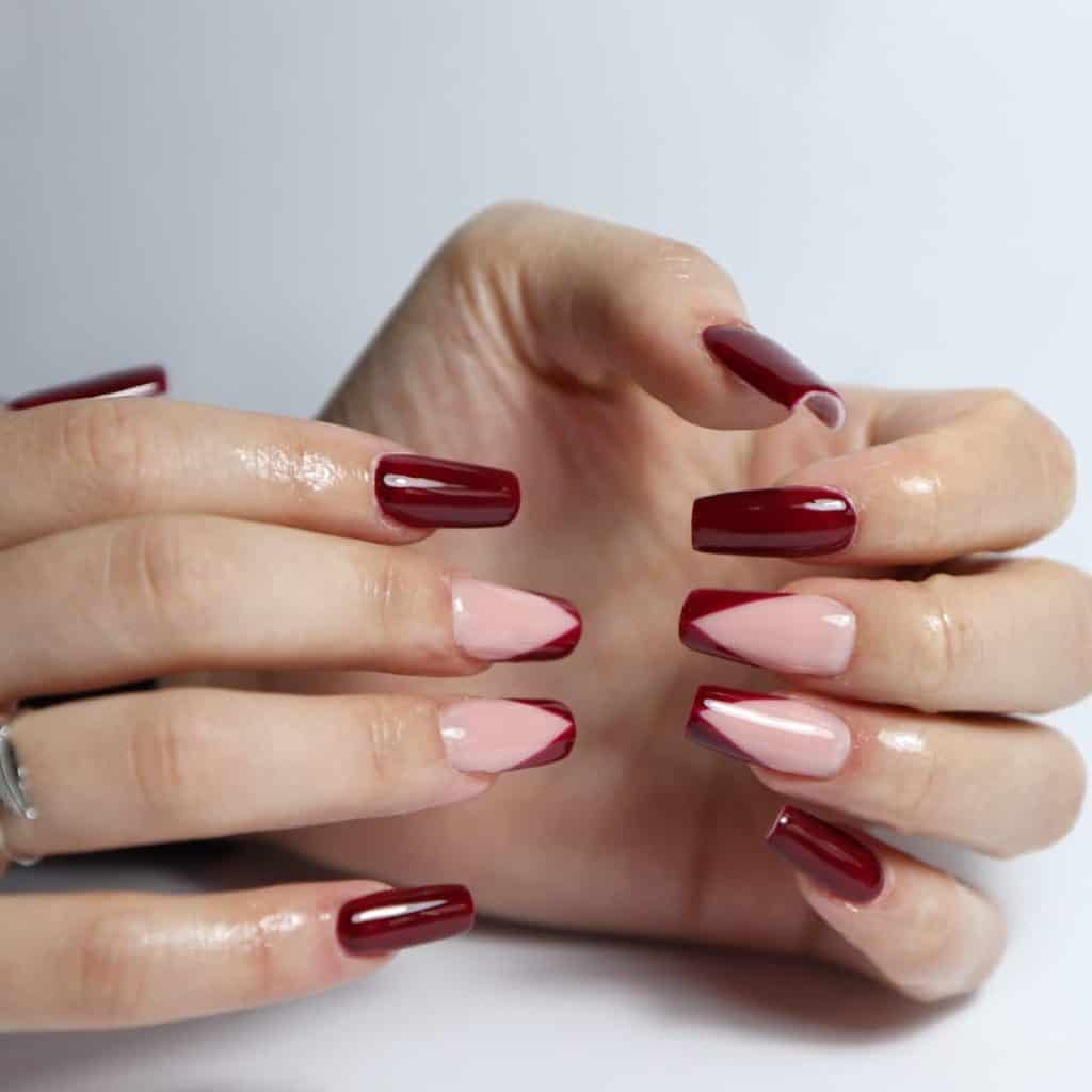 A woman's hands with long square nails painted in a sumptuous burgundy color, with the accent nails in soft peach accent nails