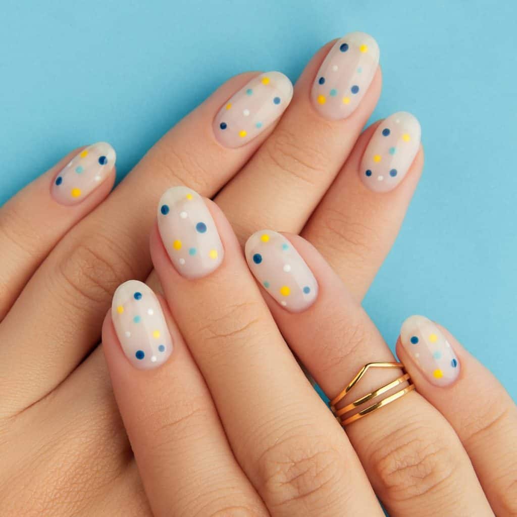 A woman's hands with milky white oval nails with polka dots in cute blue, happy yellow, and crisp white