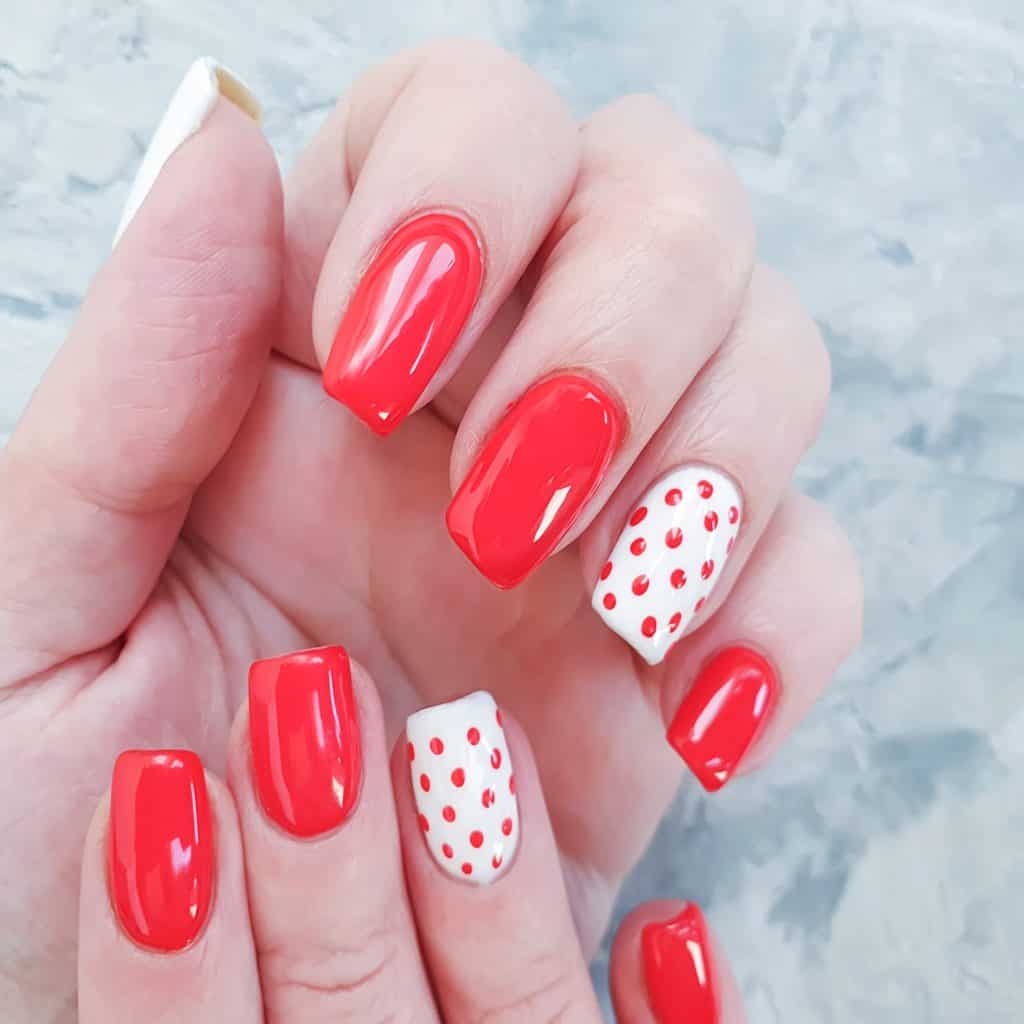 a woman's nails with mani featuring glossy red nails and an accent nail in white with red polka dots