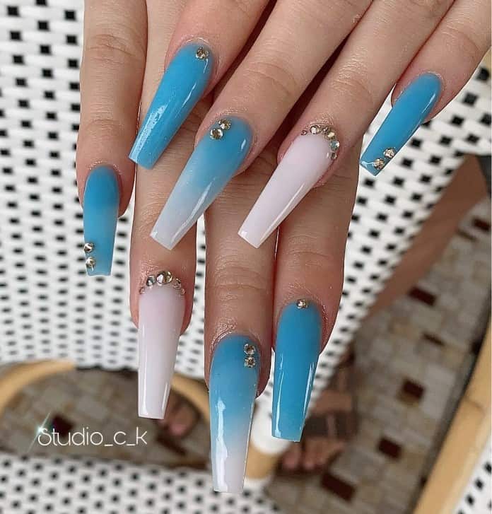A woman's hand with pale blue ombre accent nails dotted with silver rhinestones