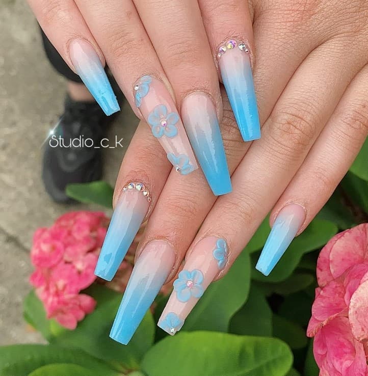 A woman's nails with pastel-blue-and-nude ombre nails have delicate 3D flowers and rhinestones