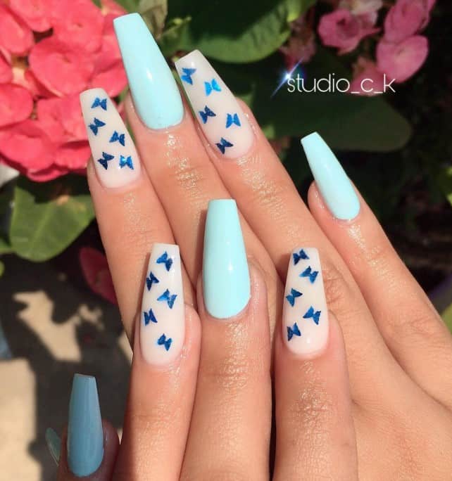 A woman's nails with dark blue butterflies onto matte pale nude nails