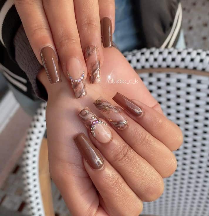 brown colored nails while two of the nails have a clear base with brown marble designs, pretty rhinestones, and silver foil