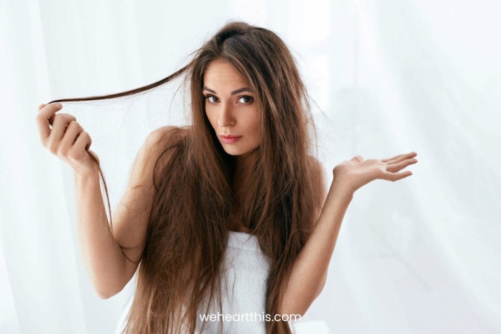 a woman with tangled hair is holding some of her hair strands while looking confused at the camera