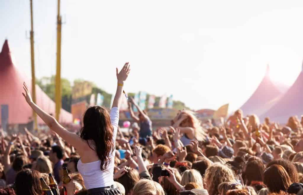 A crowd of people at a music festival with a girl wearing white longsleeves crop top enjoying