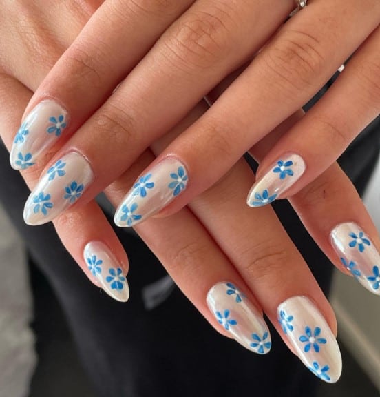 A woman's nails with blue flower petals painted onto a shimmery white base