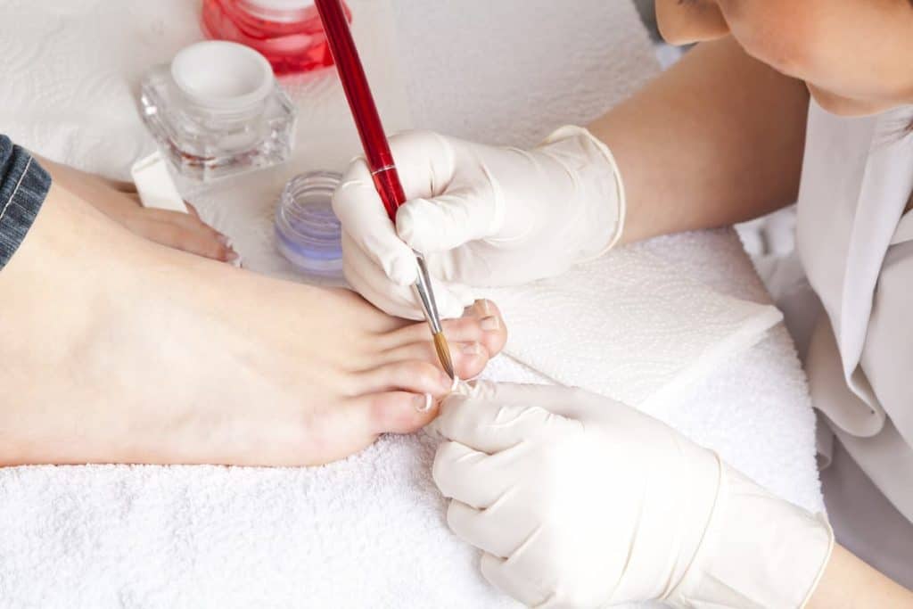 A woman getting acrylics for her toenails at a nail salon where nail tech is wearing a white gloves.