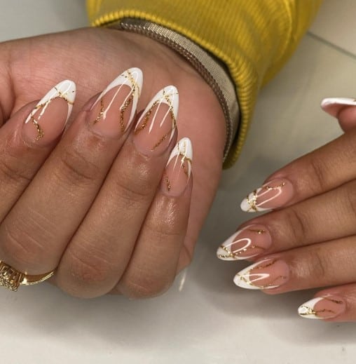 A woman's hands with pink nude base and white french tips with sporadic lines of gold drawn over each nail create an abstract theme