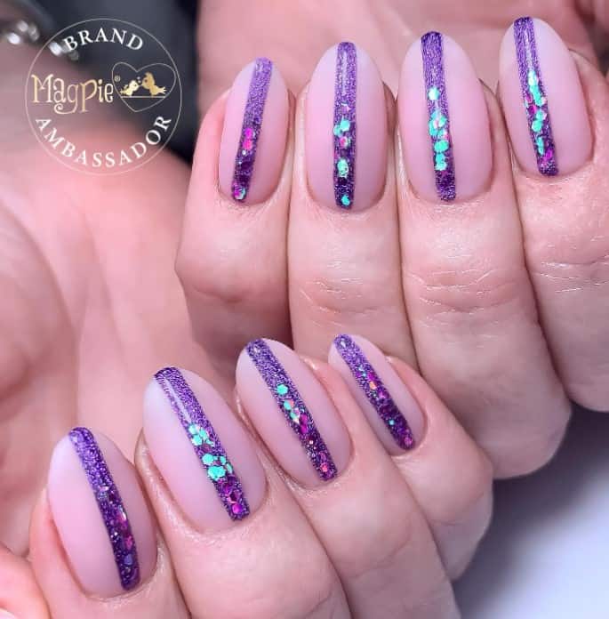 A woman's nude pink nail's base with bold violet line has a sandy, sparkly, and iridescent effect