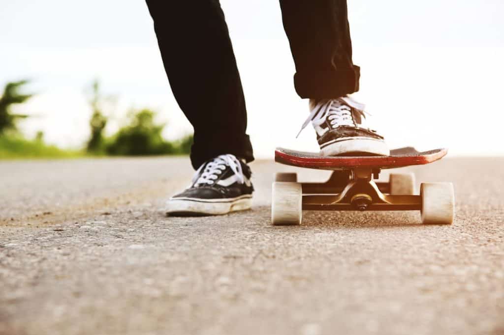 A person wearing dark jeans and vans sneakers is riding a skateboard on a road.