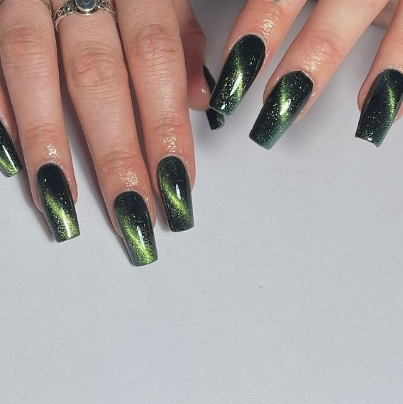 A woman's nails with light green magnetic particles create a mesmerizing cat-eye nail design against the dark background