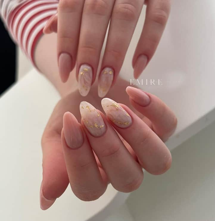 A woman's hands marbled nails with randomly scattered gold foil look great alongside the classic nude-colored nails