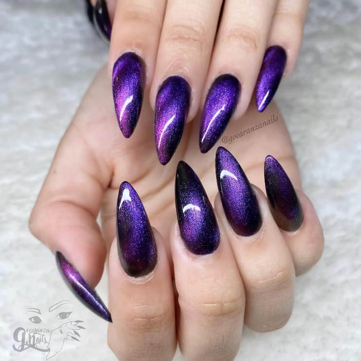 A woman's hand with stunning purple cat-eye design against a black base, glowing like a sophisticated amethyst gem nails