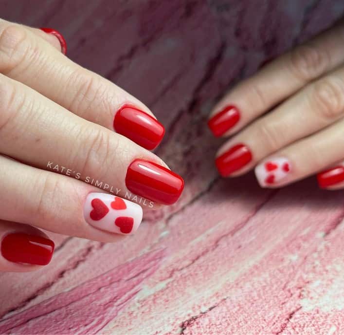 A woman's red nail set showcases white accent nails painted with matte red sugar hearts
