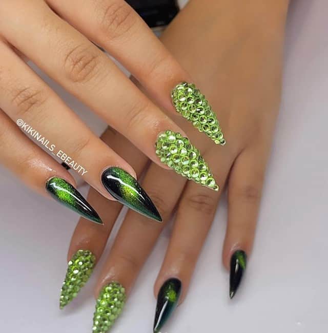 A woman with extra long stiletto nails captivate with their black and green cat-eye nail design and light green gems on accent nails