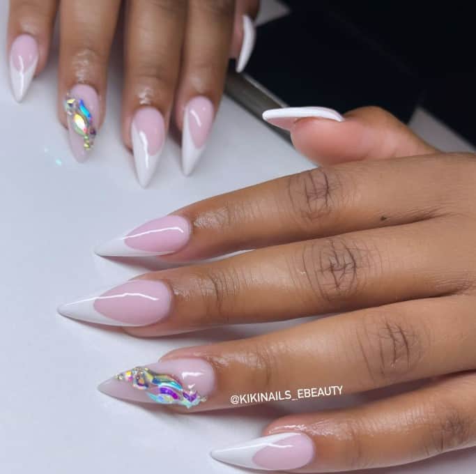 A woman's stiletto nails in French mani boldly display colorful jewels that strongly contrast the color of the nail base