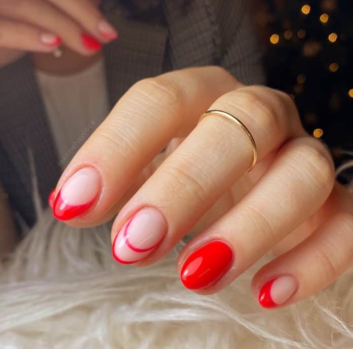 A woman's nails with red French tips on a nude base and accent the manicure by painting one nail in full color and one nail with an outlined double French tip design