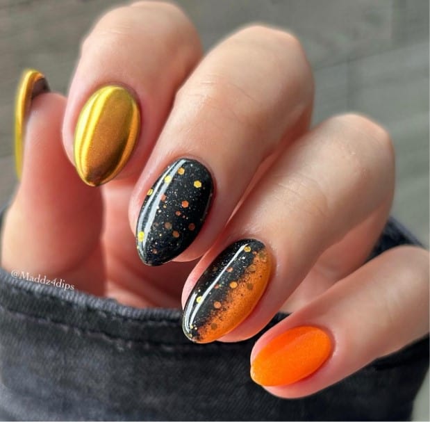 A woman's mid-length oval nails featuring the captivating trio of orange, black speckled, and glistening gold