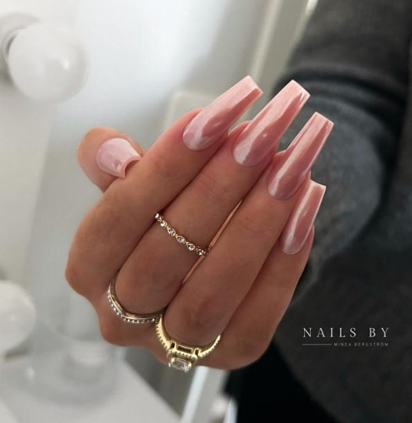 A woman's pinkish nude base nails with subtle shimmer on long, square nails with a ring on it.