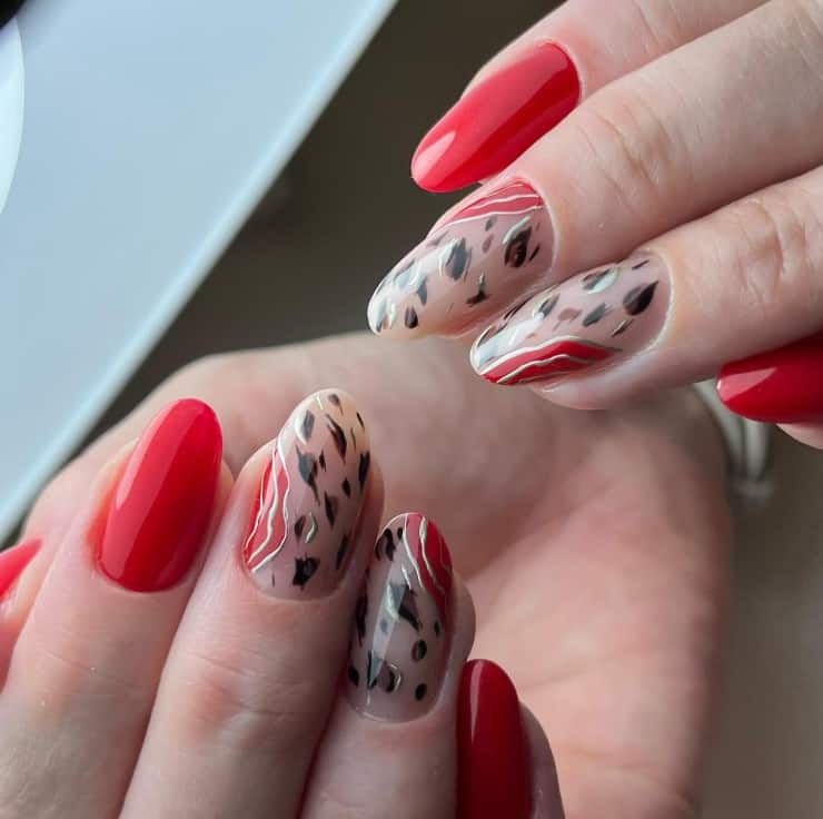 A woman's bright red set with accent nails that feature short, brown, black, and brass abstract cheetah print on a nude-colored base