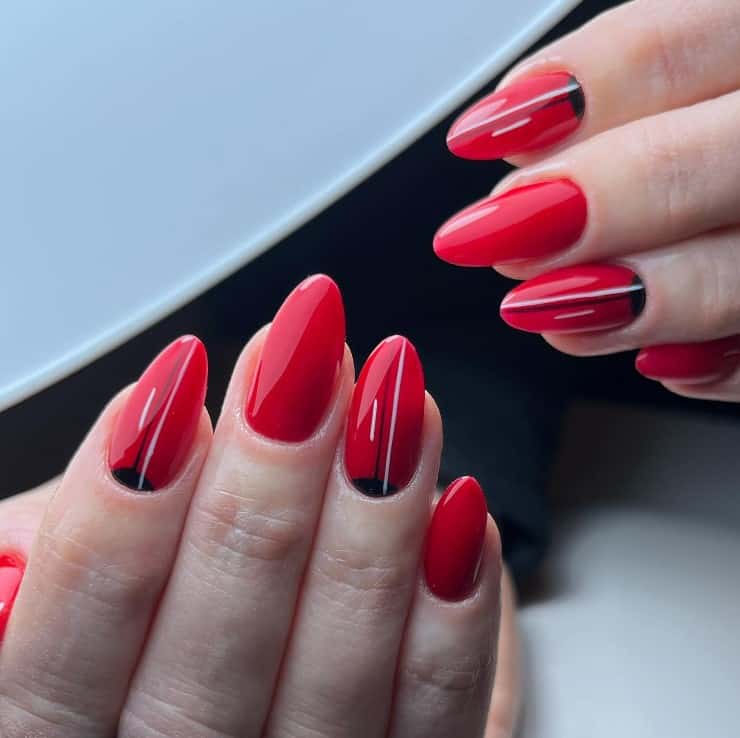 A woman's red nails where accent nails decorated with black reverse French tips with thin black and white vertical lines