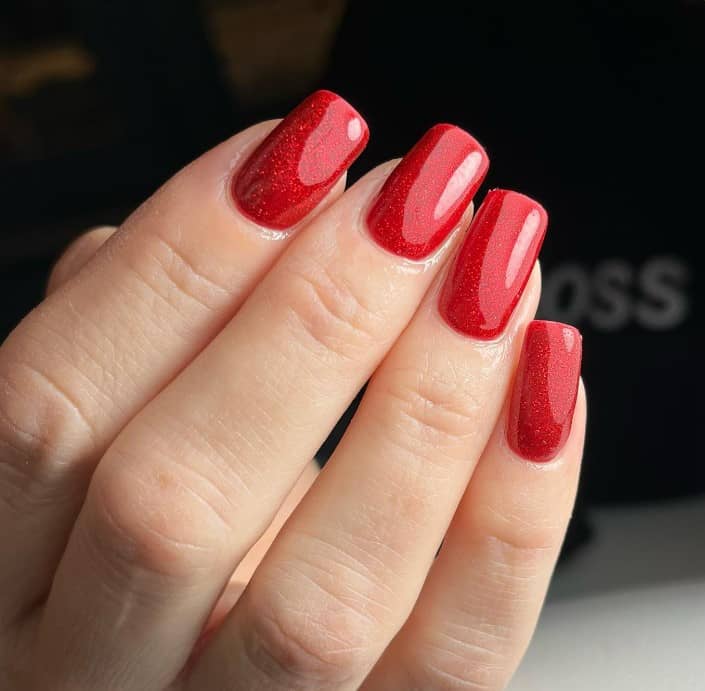 A woman's square nails use a glittery bright red polish