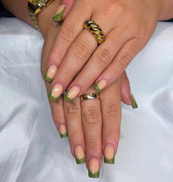 A woman's hands with sage green and dark green nail polish over pale cream nails to evoke the look of croc skin as French tip accent