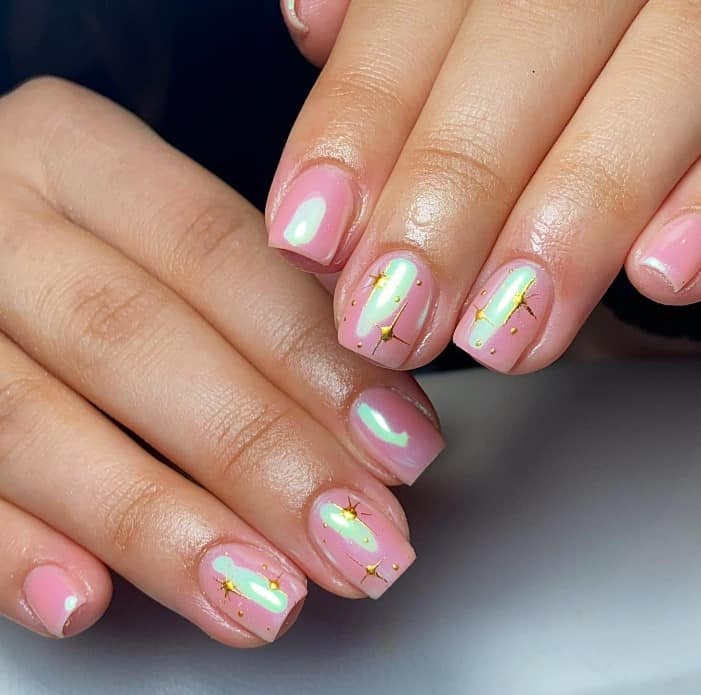 A woman's light pink nails with gold North Stars and rhinestones for accent