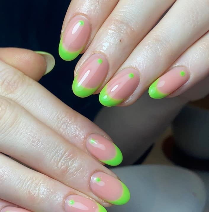 A woman's pink nails and neon green french tips with dots on them.