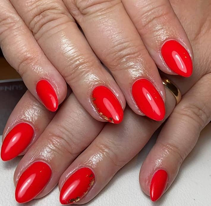 A woman's plain red nails by including a sideways French tip accent using gold flecks