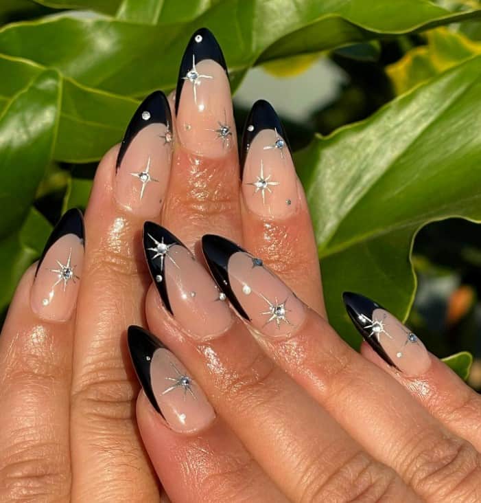 A woman's hands with neutral base and black tips and sparkling stars design