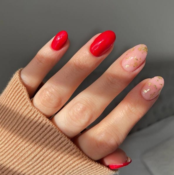 A woman's bright red nails with nude accent nails embellished with flecks of gold foil