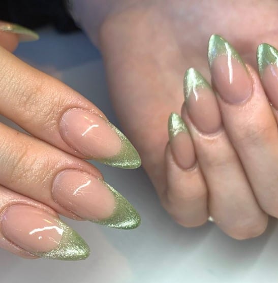 A woman's hands with green french tips on a nude nails with glittery effect