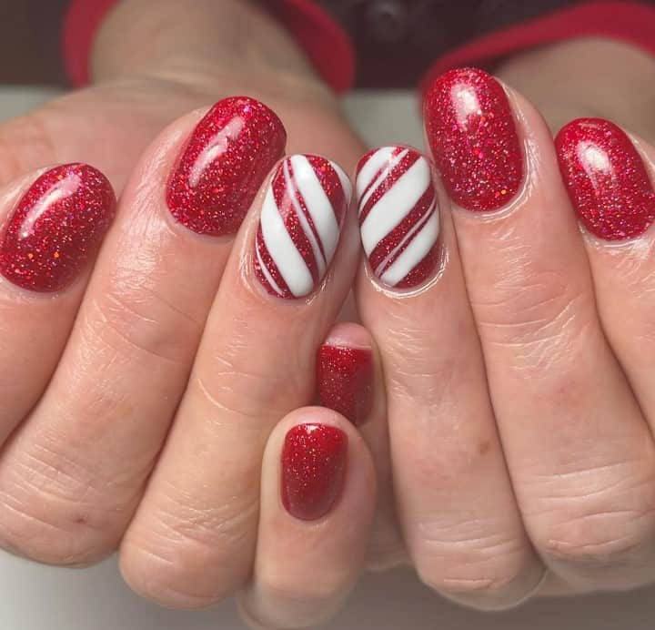 A woman's hands with red glitter nail design with accent nails painted with diagonal lines in white nail polish