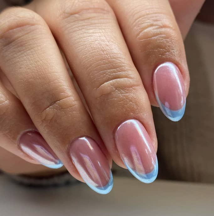 A woman's hand with icy glazed nails feature baby blue French tips on a nude base and topped with a shimmery topcoat