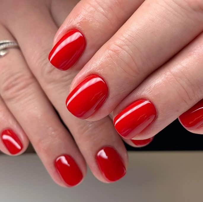 A woman's red nail polish topped with gloss