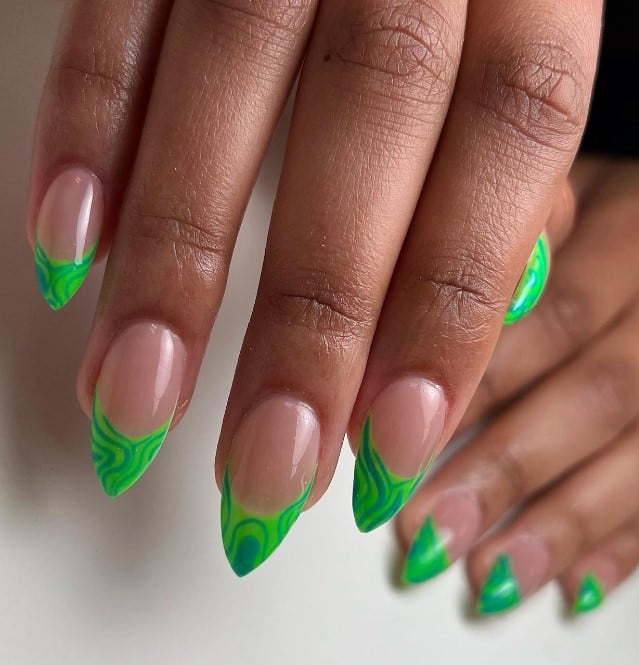 A woman's nails with blue swirls and squiggles over the green French tips
