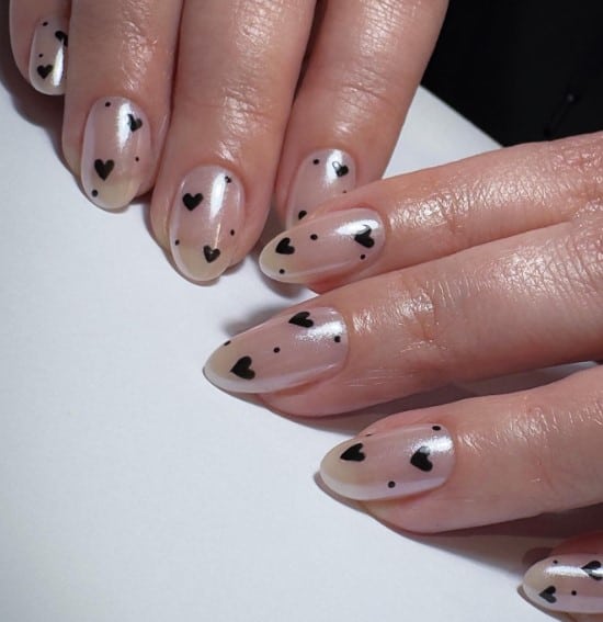 A woman with tiny black hearts and dots over the iridescent nude base nails.