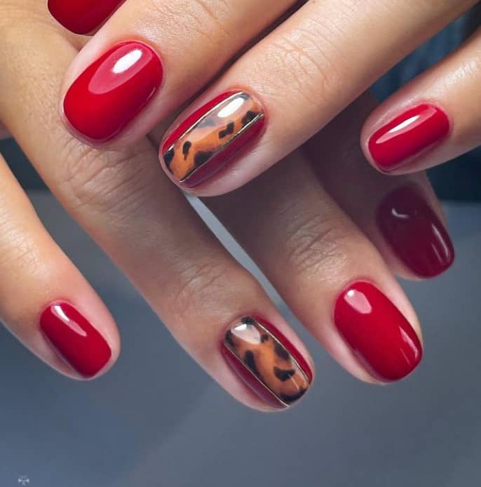 A woman's glossy red manicure creates a nice contrast against accent nails that feature a tortoiseshell pattern delicately framed by thin gold outlines on the adjacent red nails