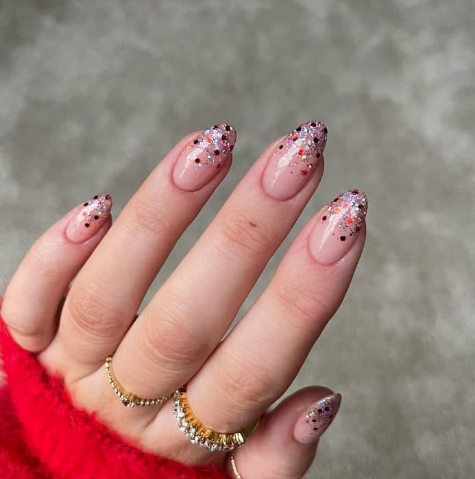 A woman wearing a red sweater with French tips feature sparkly confetti accents nails.