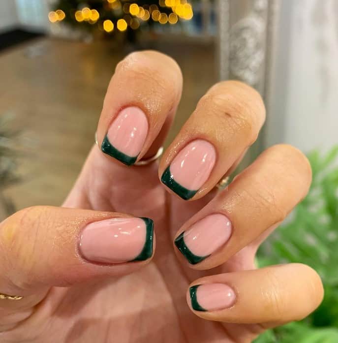 A woman with dark green French tip nails over a nude pink base manicure.
